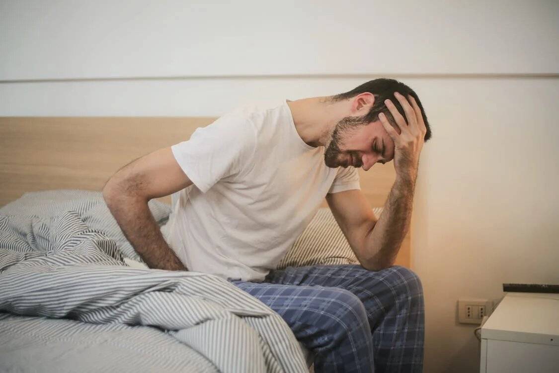 Man in sleepwear sitting on the bed suffering from headache