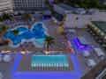 Ein weitläufiger Poolbereich mit großem, unregelmäßig geformtem Becken, Dachpool mit blauer Beleuchtung sowie einer beleuchteten Poolbar.