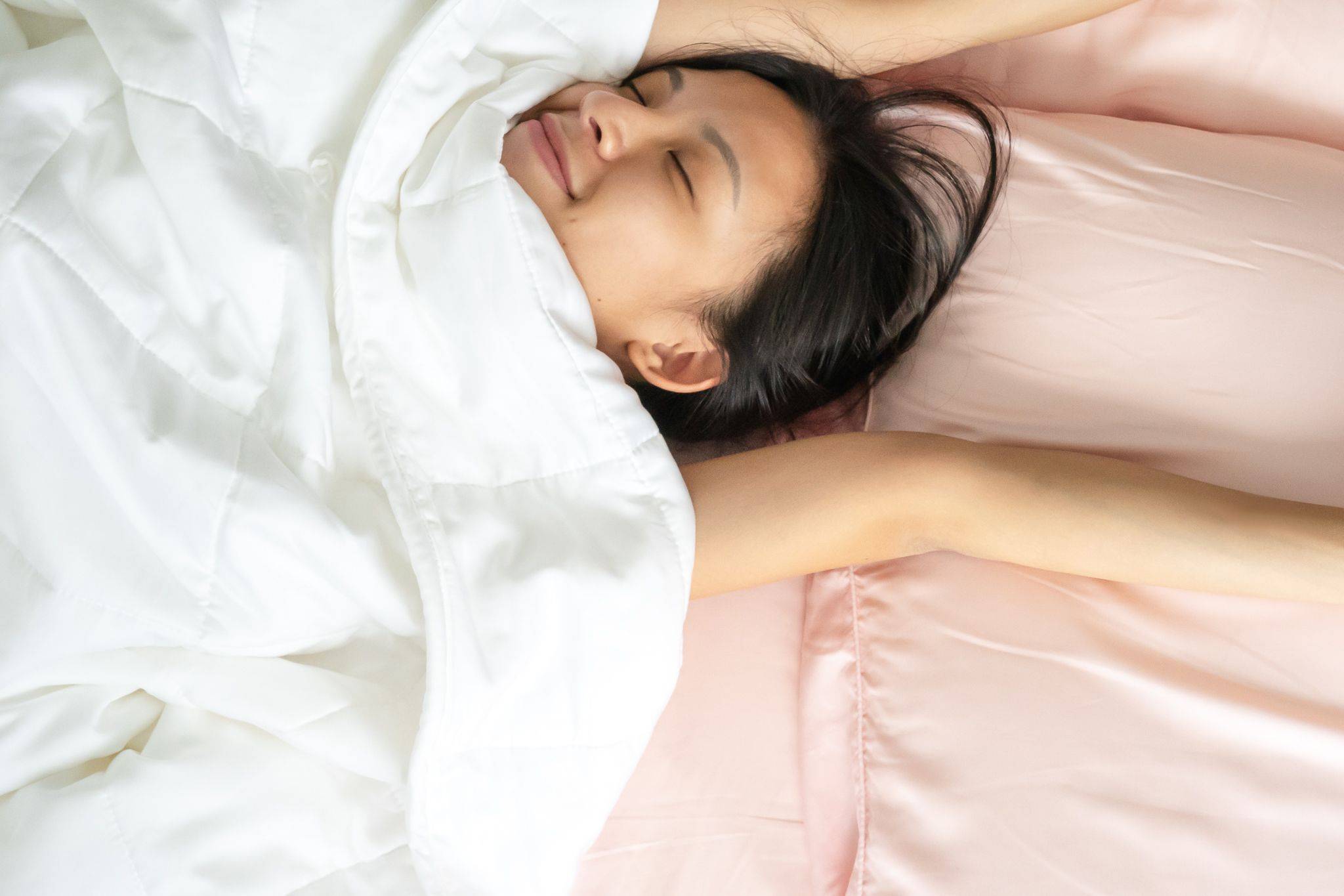 Smiling girl stretching on bed under Weavve's tencel lyocell duvet in white