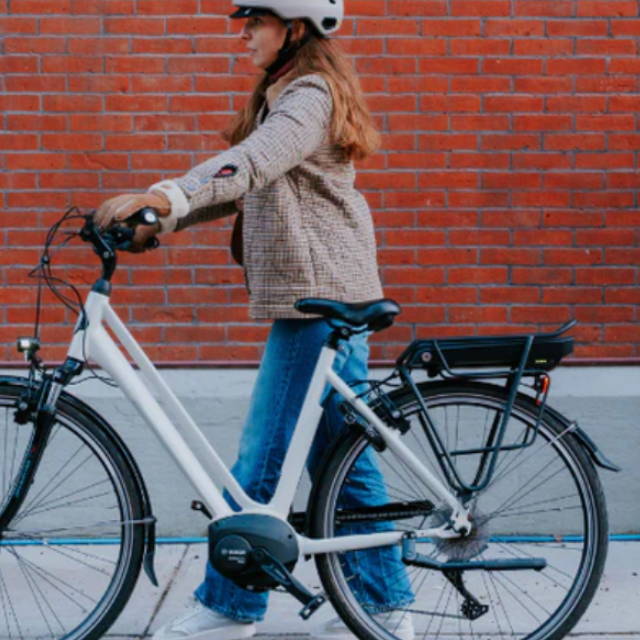 a woman walking next to an electric city bike in front of a red brick wall