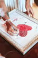 Woman signing red fingerprint heart guest book print in frame clicking this photo leads to the wedding collection