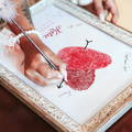 close up of woman's hand holding pen and signging fingerprint wedding guest book alternative print