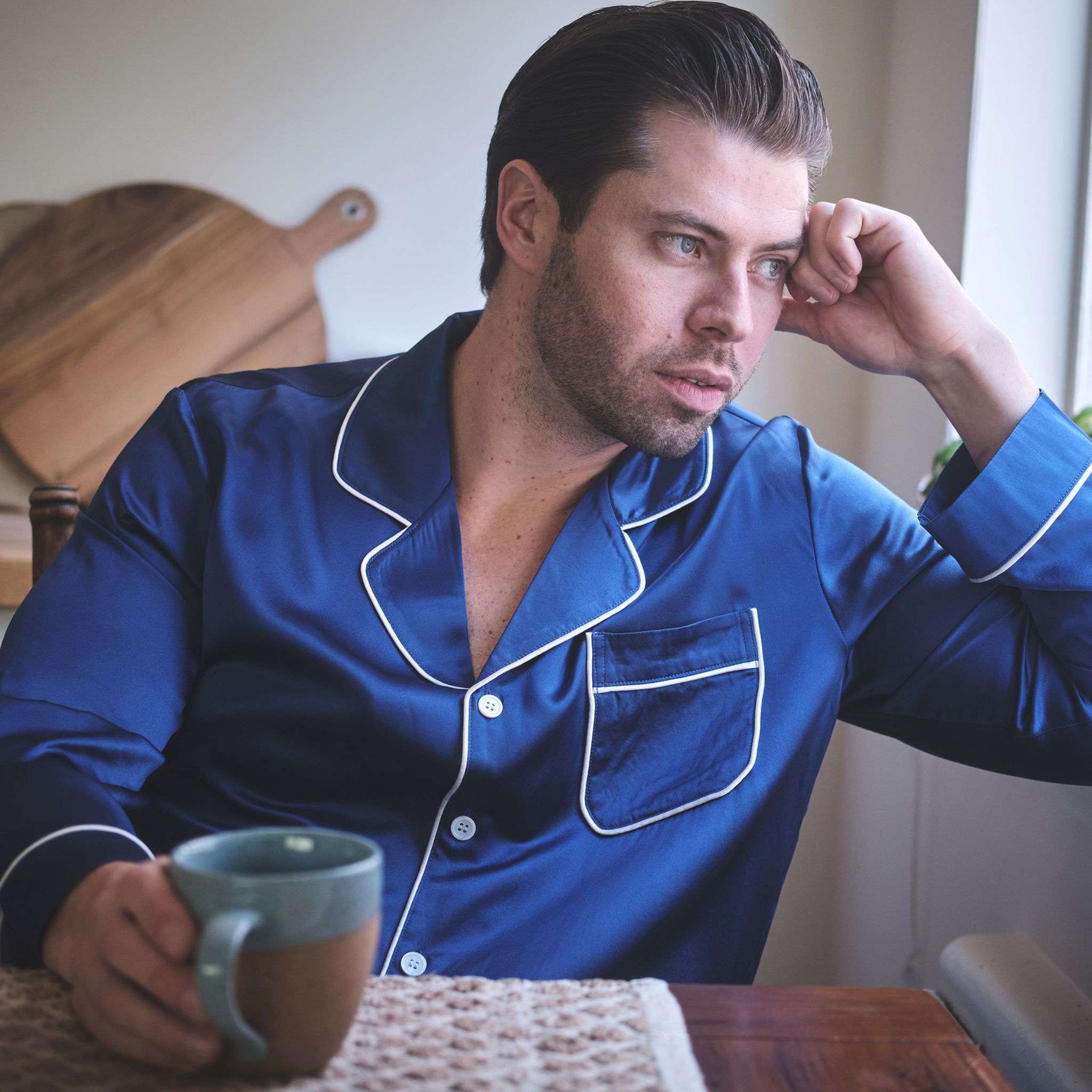 photo of a model wearing midnight blue silk pajamas and looking out the window 