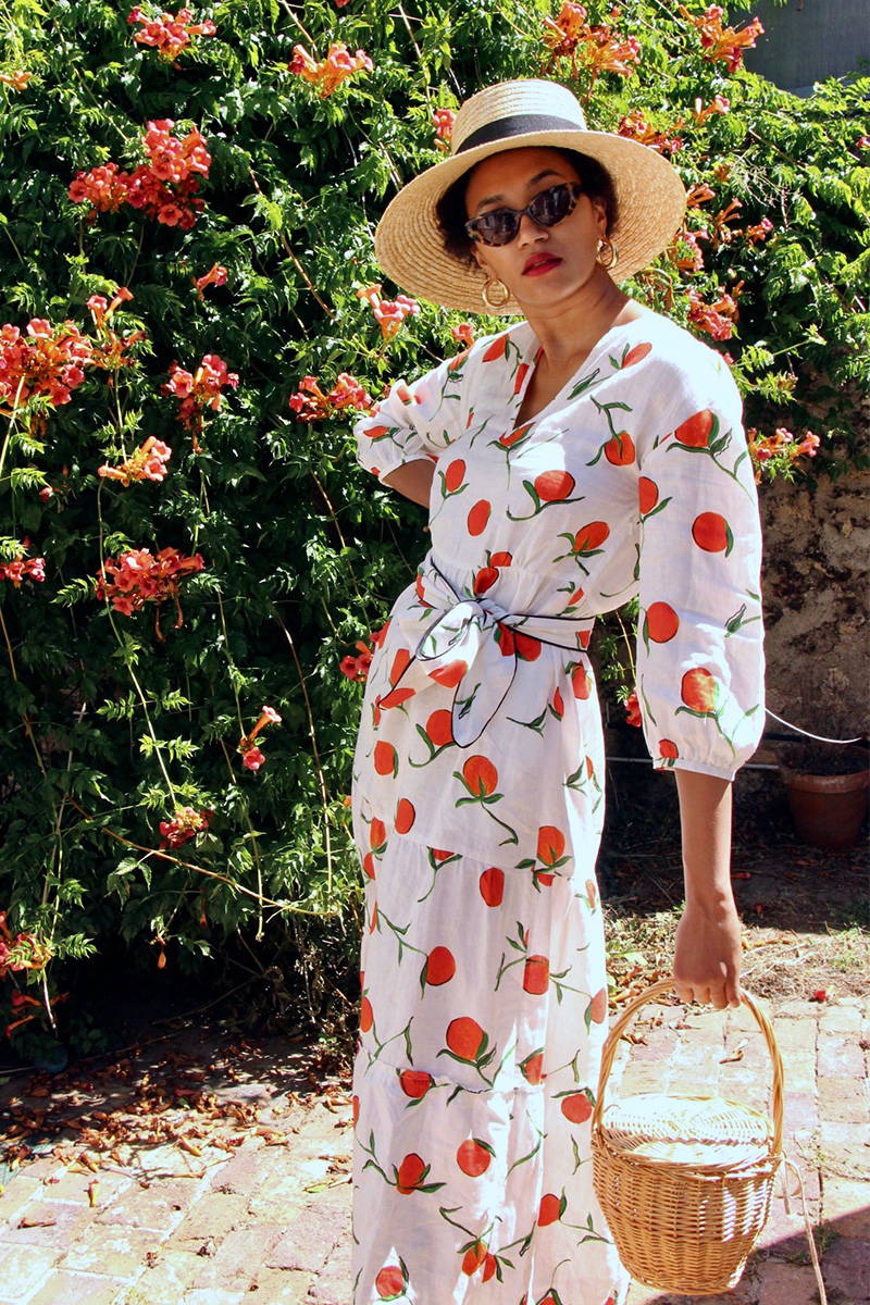 Lena Farl wearing YOLKE's Orange Babushka Dress wearing a sun hat and standing amongst flowers