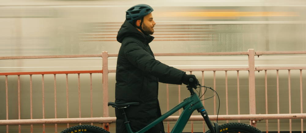 a man walking an electric mountain bike as a subway goes past in new york city
