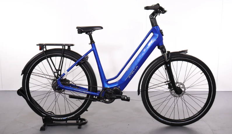 Stella Vicenza e-bike met lage instap in blauw, zijaanzicht op witte achtergrond – elektrische stadsfiets met middenmotor, bagagedrager, verende voorvork en gesloten kettingkast