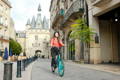 Femme à vélo électrique roulant dans le centre de Bordeaux avec un château derrière