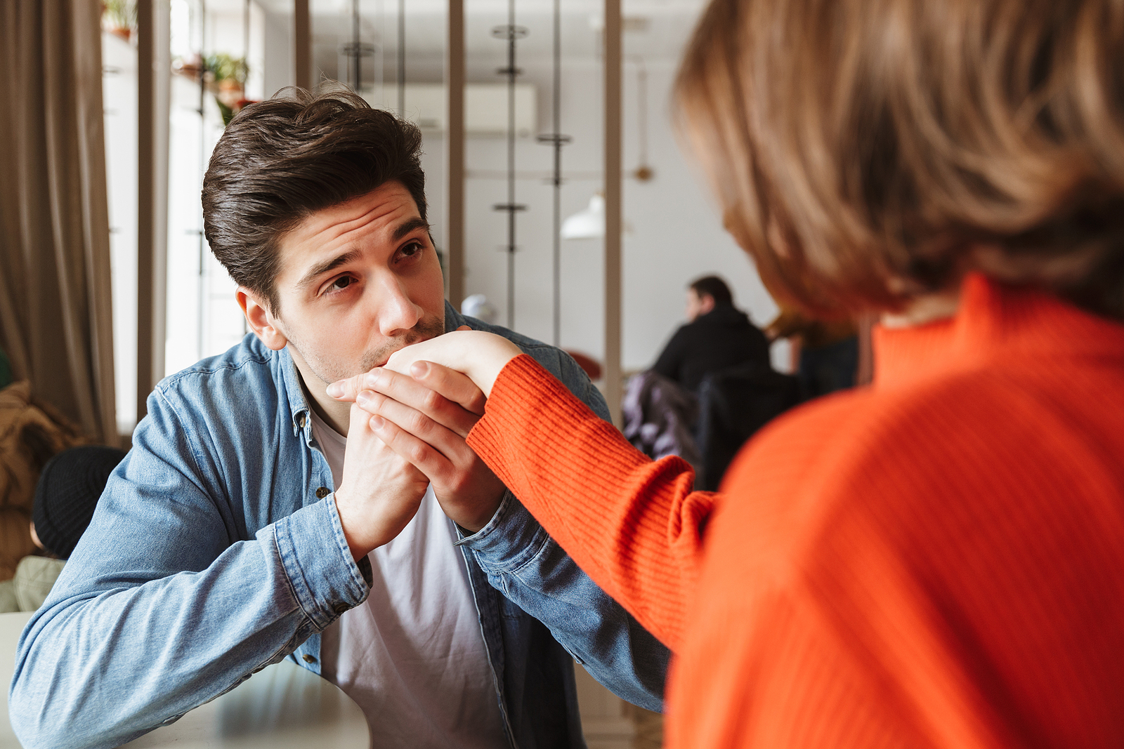 Loving couple resting in restaurant while handsome guy kissing hand of his brunette girlfriend.