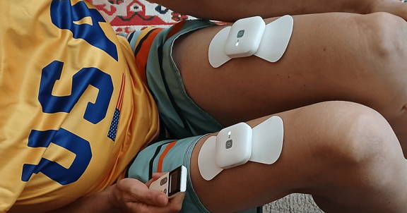 Woman wearing Wellue wireless TENS pods on the upper and lower back with four independently controlled therapy channels displayed.