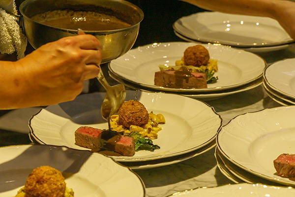 Wagyu beef, meatball, elbows pasta and salad being plated.