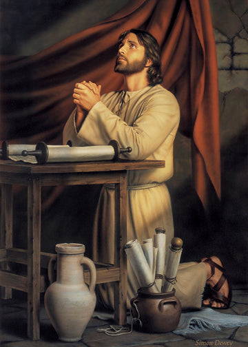 Jesus kneeling at a table with a scroll laid out in front of Him. More scrolls are in a vase on the ground next to Him.