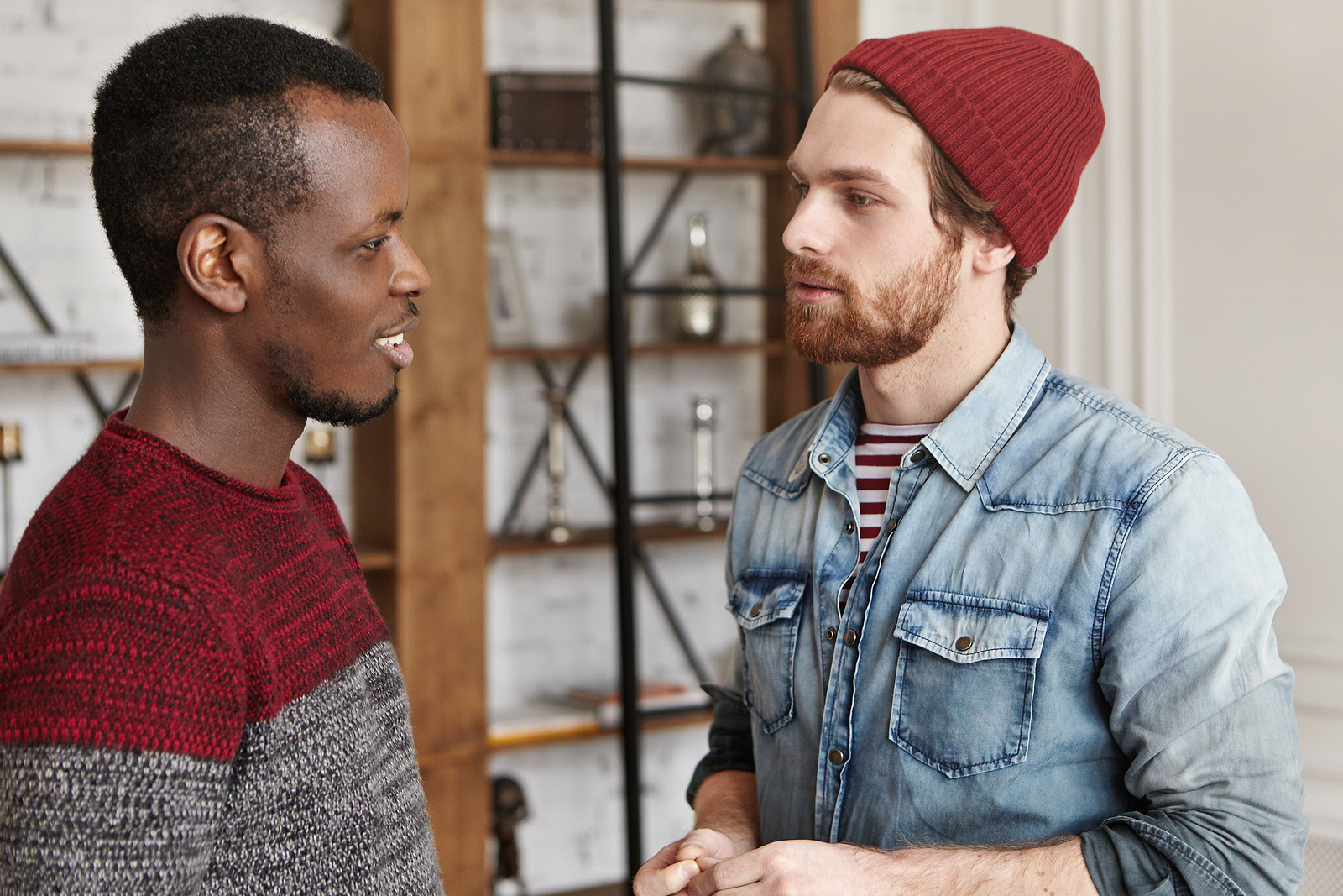 Two young men talk to eachother. One man is smiling while the other looks more seriously at him.