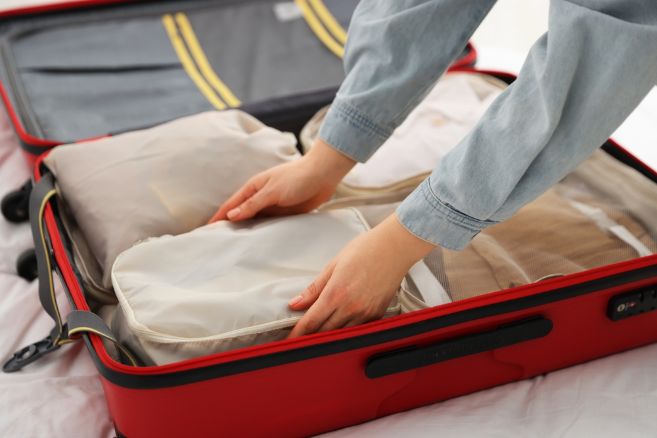Woman putting packing cube into suitcase indoors, closeup