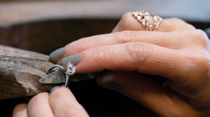 Main de joaillière sur un banc de joaillier qui travaille sur un bijou.