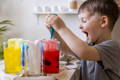 Excited young boy experimenting with colorful water and droppers, engaged in a fun and playful science activity at home.
