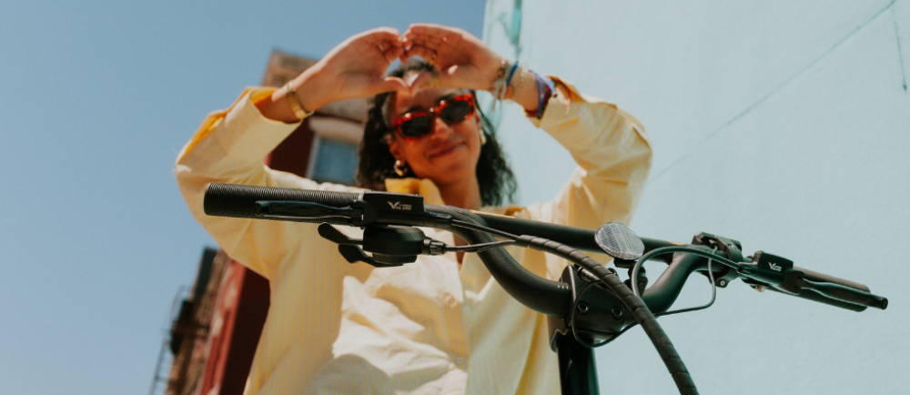 A woman making a heart with her hands while on an ebike