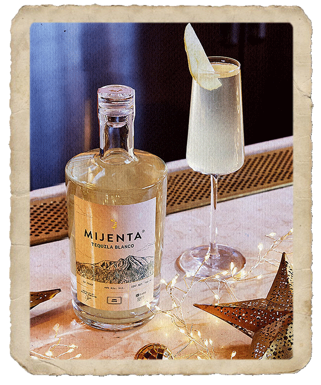 Tall glass with prepared cocktail sided by a Mijenta Tequila Blanco bottle.