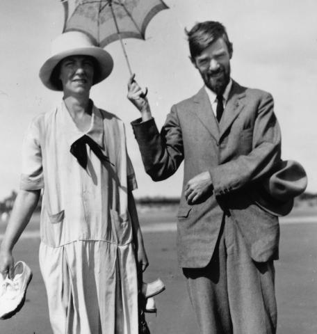 D.H. Lawrence holding an sun umbrella standing next to a woman.