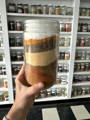 The various ingredients for making homemade Sazon all in a large glass jar, separated by layers of each spice