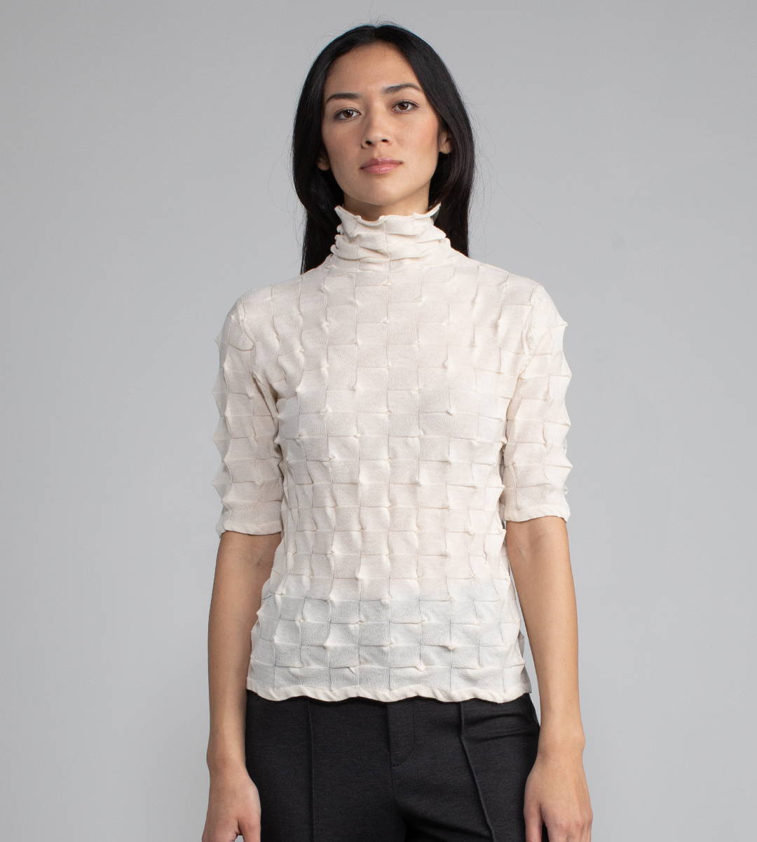 Woman wearing a white t-neck origami knit top.