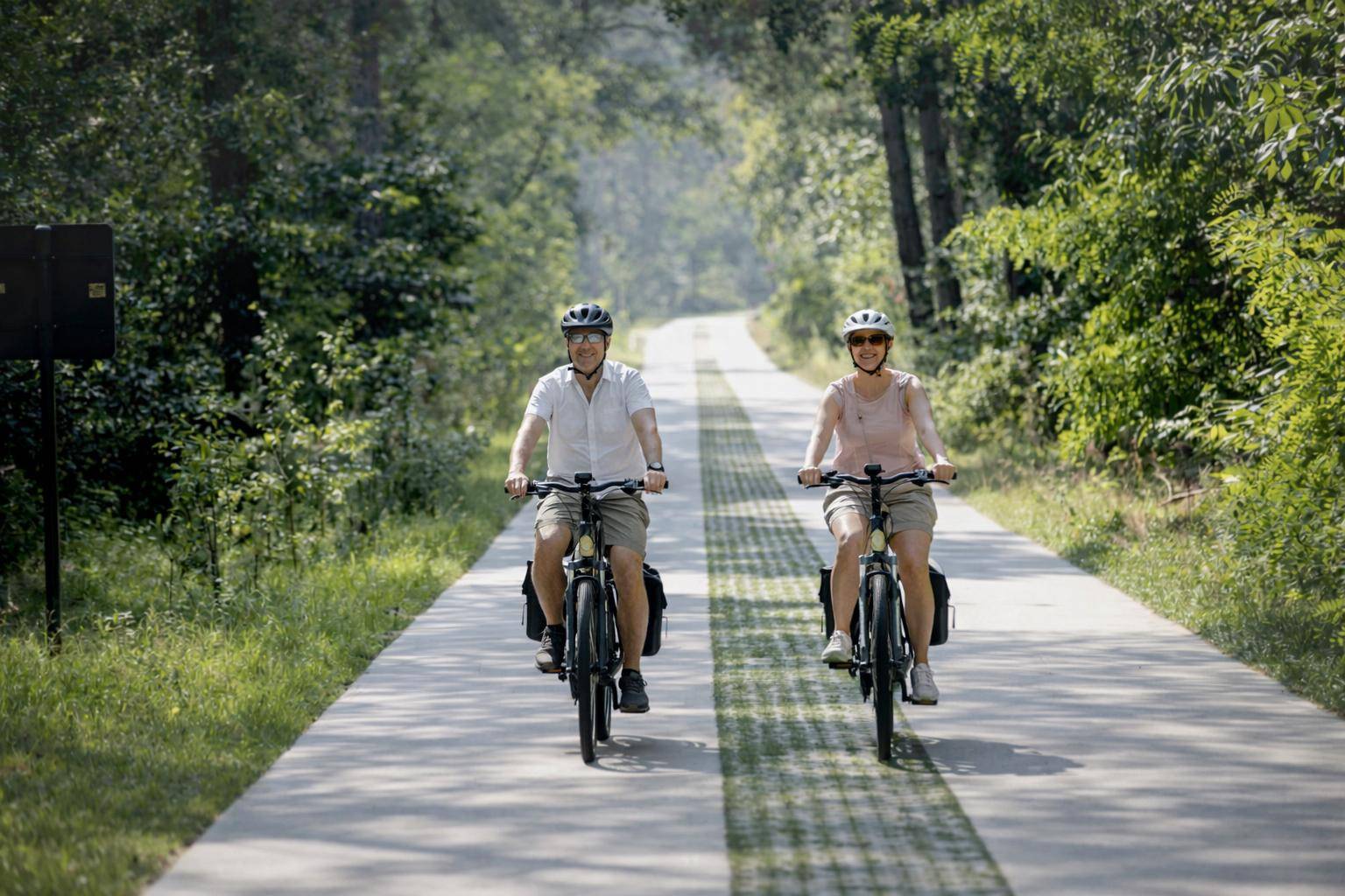 Twee fietsers op elektrische fietsen rijden op een breed fietspad door de Kempen nabij Antwerpen, omringd door bomen en groen