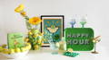 A display of cocktail themed items in yellow and green against a white background. A white bowl with yellow lemons in relief around the edge with leaves and flowers, a book 'Sip and Sensibility'. A large vase with a lemon tree with large lemons in relief, yellow silk flowers in it. A art print in a poster style of a Margarita glasee, cocktail glasses, mixers, lemon ice cube tray and a bright green tray with the words Happy Hour.