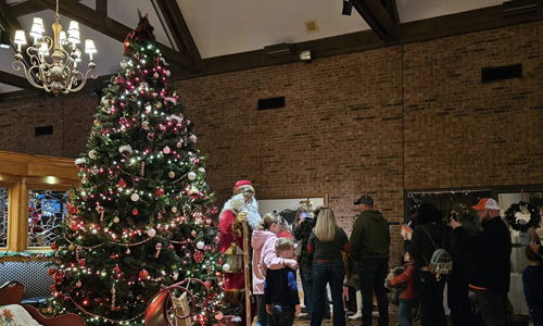 A festive indoor scene features a decorated Christmas tree, cozy couch, and a joyful group waiting to meet Santa.