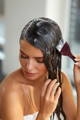 brunette woman applying hair mask on hair with brush