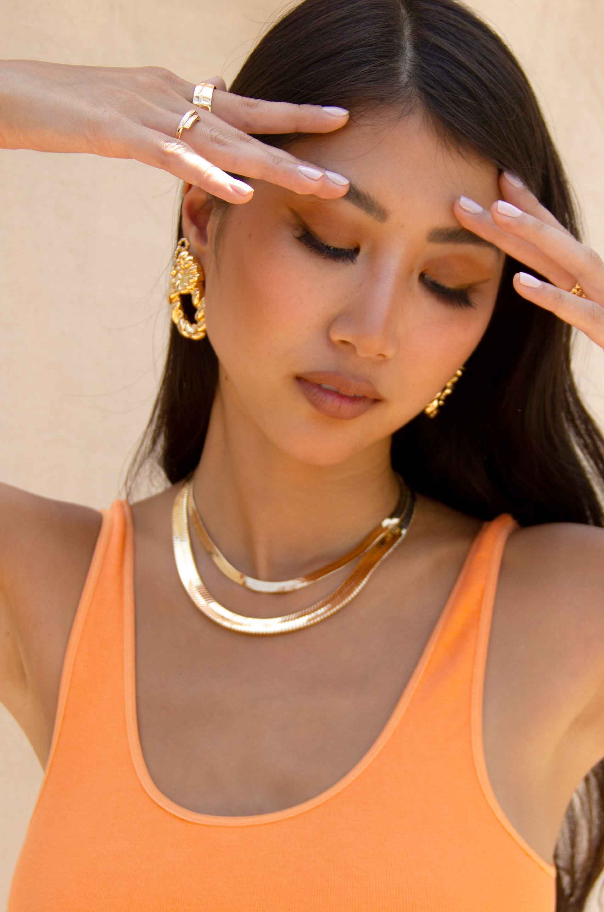 A model wearing ettika 18k gold plated necklaces and statement earrings