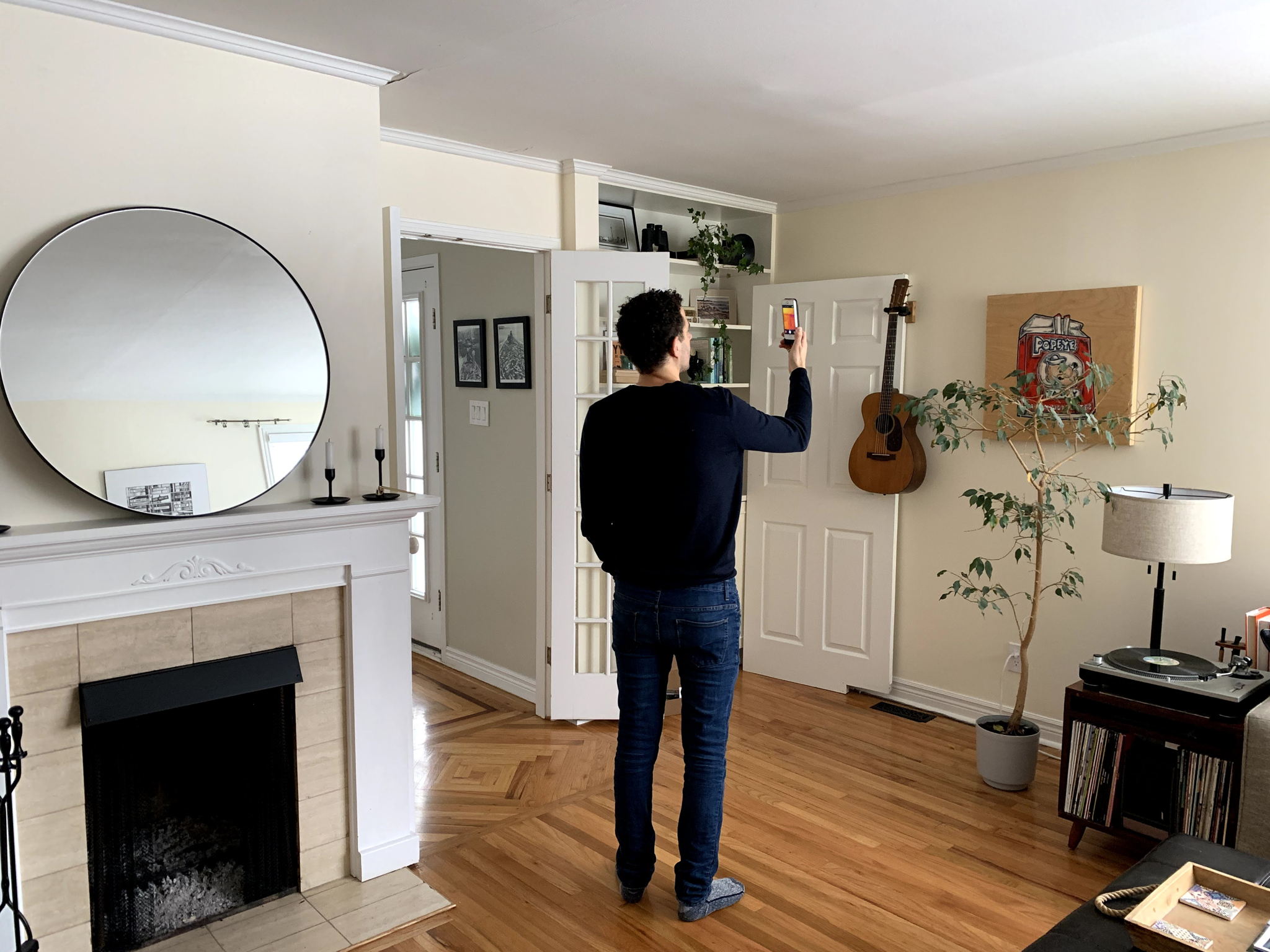 man in living room hold up a smartphone with wall temperature reading