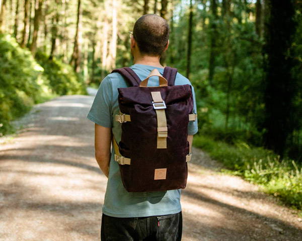 Man wearing burgundy organic cotton canvas backpack from men's UK sustainable clothing brand The Level Collective