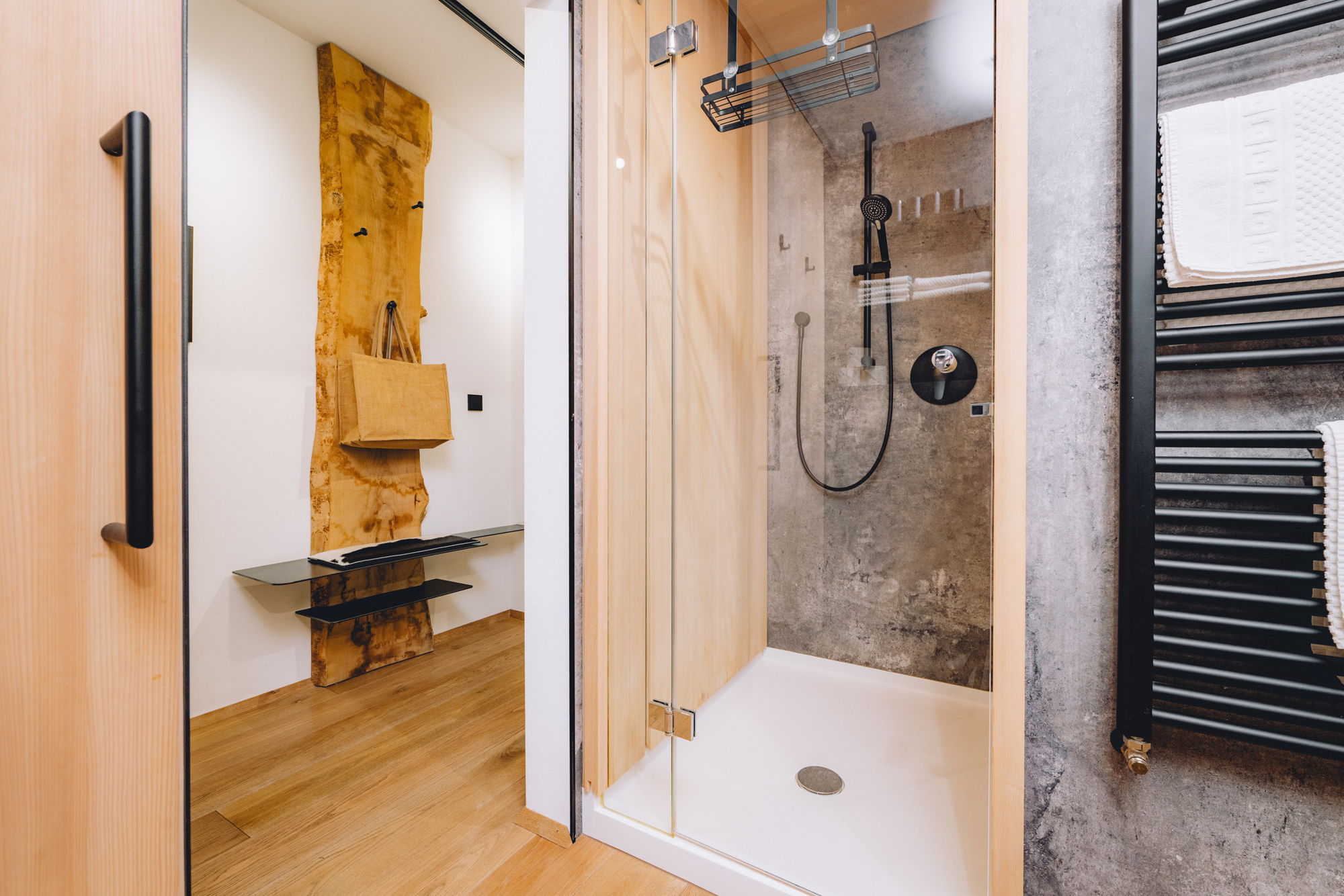 Links Blick auf den Flur, rechts eine moderne Dusche mit Holz- und Steinwänden, ganz rechts eine Wandheizung.