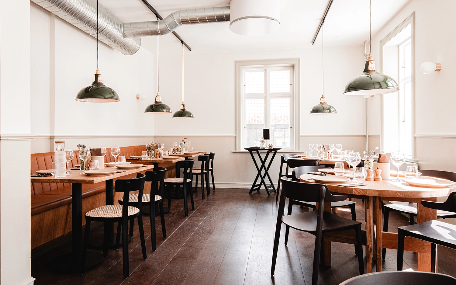 Large Green Coolicon Pendant Lampshades hanging inside a Scandinavian restaurant with wooden tables, chairs and floors.