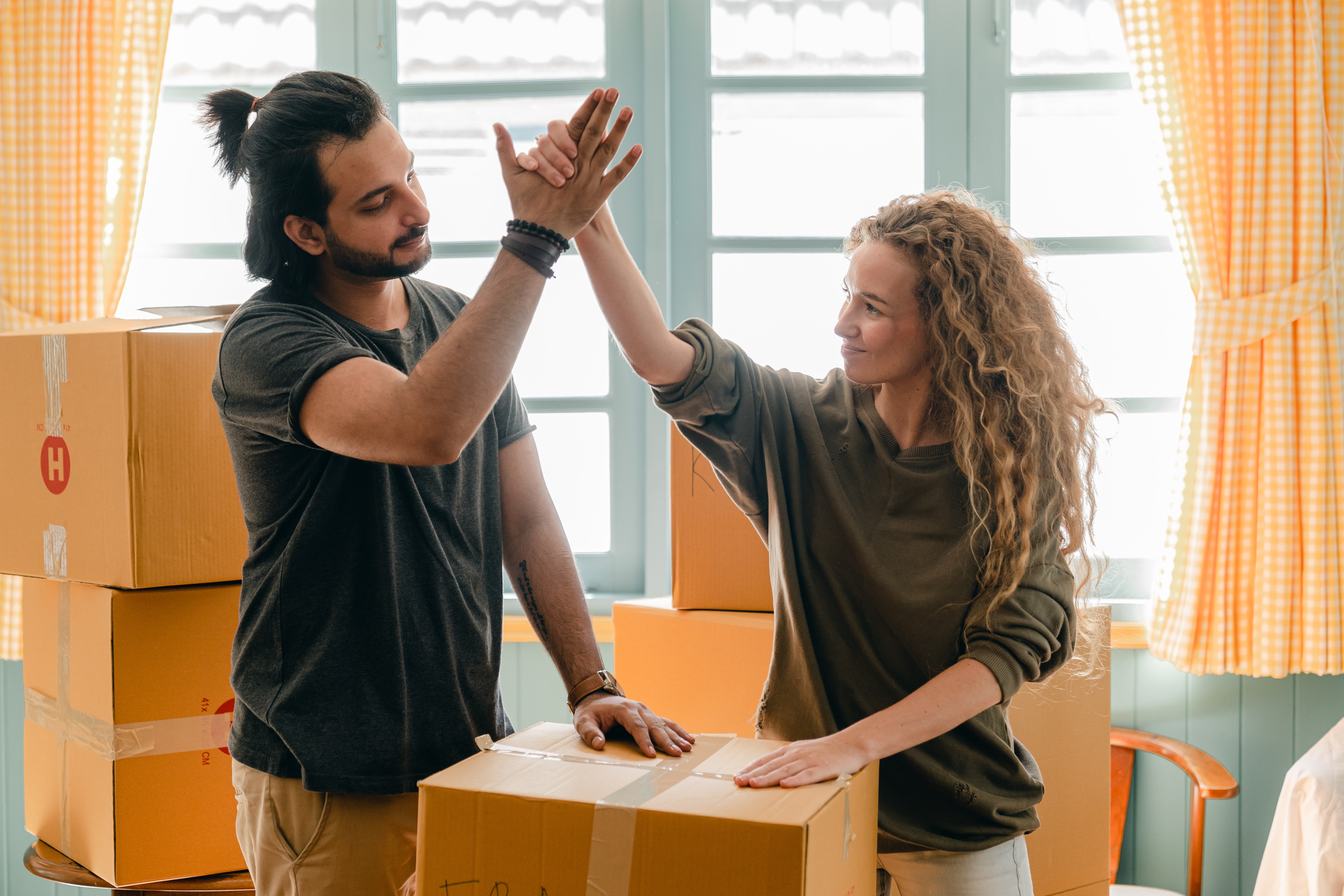 A man and woman both with long hair high five eachother while moving boxes in a new home.