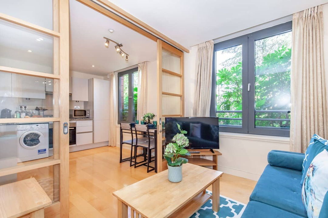 Living room with coffee table and TV facing the sofa, lovely wooden doors with large windows separates the living room and kitchen/dining room