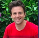Frank is shown looking into the photo and smiling. He is outside, wearing a red t-shirt.
