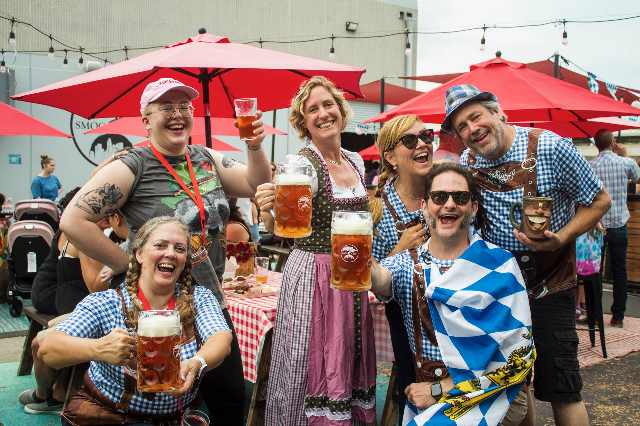 A group of people enjoying Smogtoberfest holding steins of beer and dressed in traditional Oktoberfest clothing.