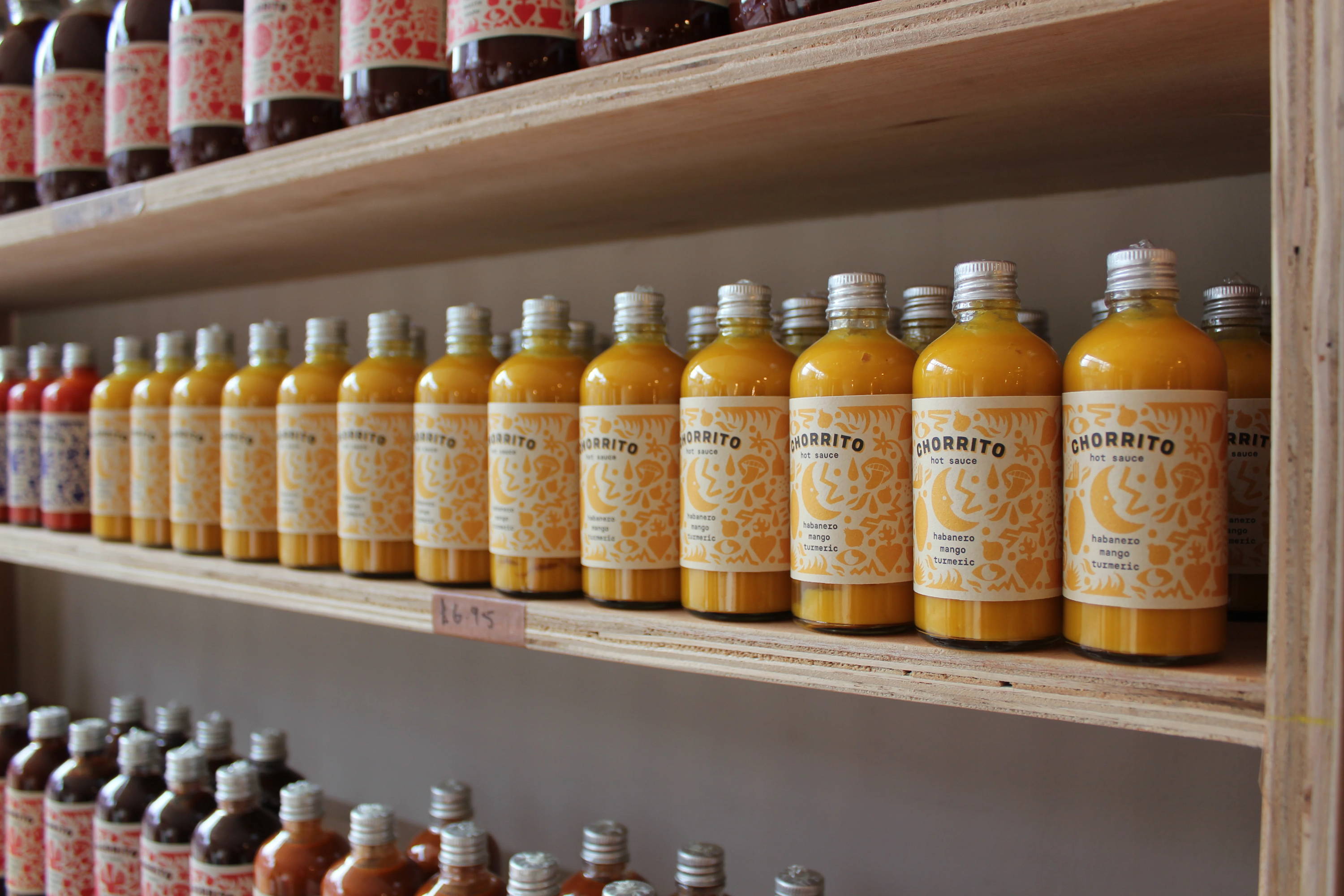 Bottles of hot sauce lining wooden shelves stacked vertically on a wall.