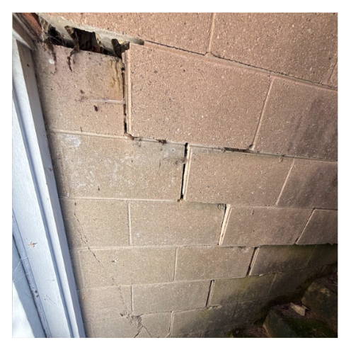 Cracked and displaced block wall with visible shifting and separation near a door frame, indicating structural damage due to grade level changes