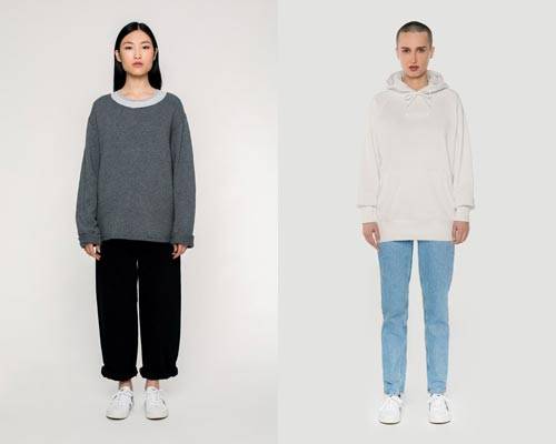 Woman wears organic cotton grey wide scoop neck jumper with rolled up wide leg black trousers and woman wears cream hoodie with light wash jeans, both from sustainable fashion brand Rotholz
