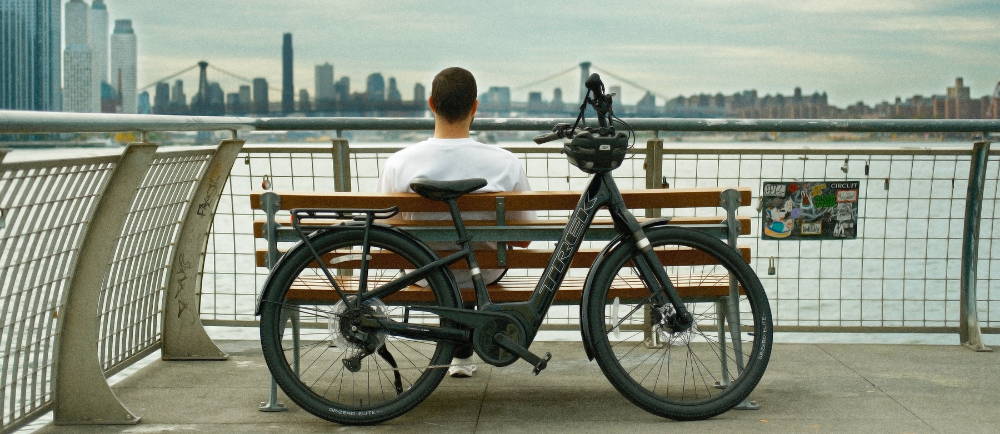 a man sitting on a park bench overlooking the hudson river with a trek electric city bike in the foreground
