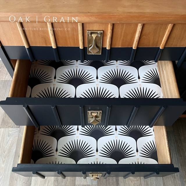 Overhead shot of drawer interiors showing black modern swan on white background wallpaper within drawers on a dresser with natural top and navy dipped painted design
