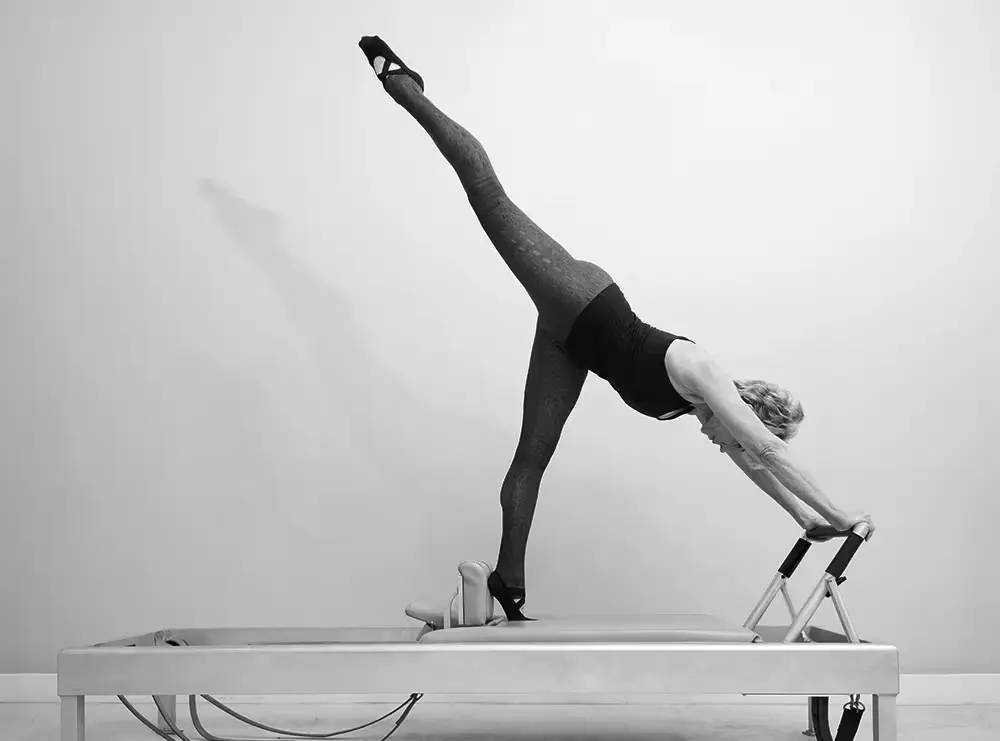 Photo of Sonje on a reformer with her one leg in the air as she is holding herself up with the foot bar