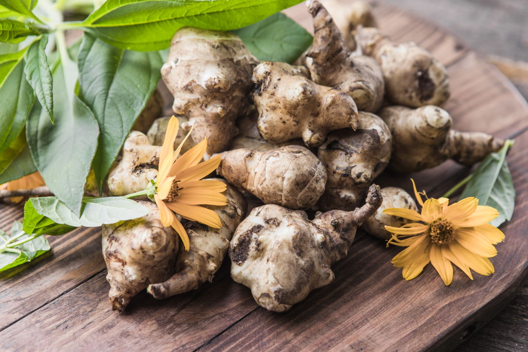 Jerusalem artichokes on a wooden board surrounded by herbs and flowers