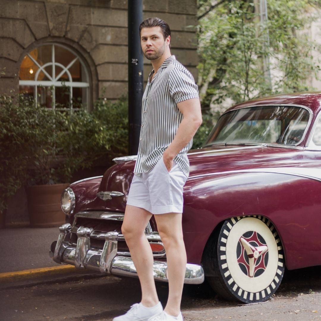 model walking on the street wearing white shoes white shorts and a short sleeve green stripe silk shirt from 1000 kingdoms