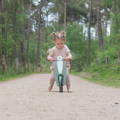 Little girl riding her green balance bike in the nature.