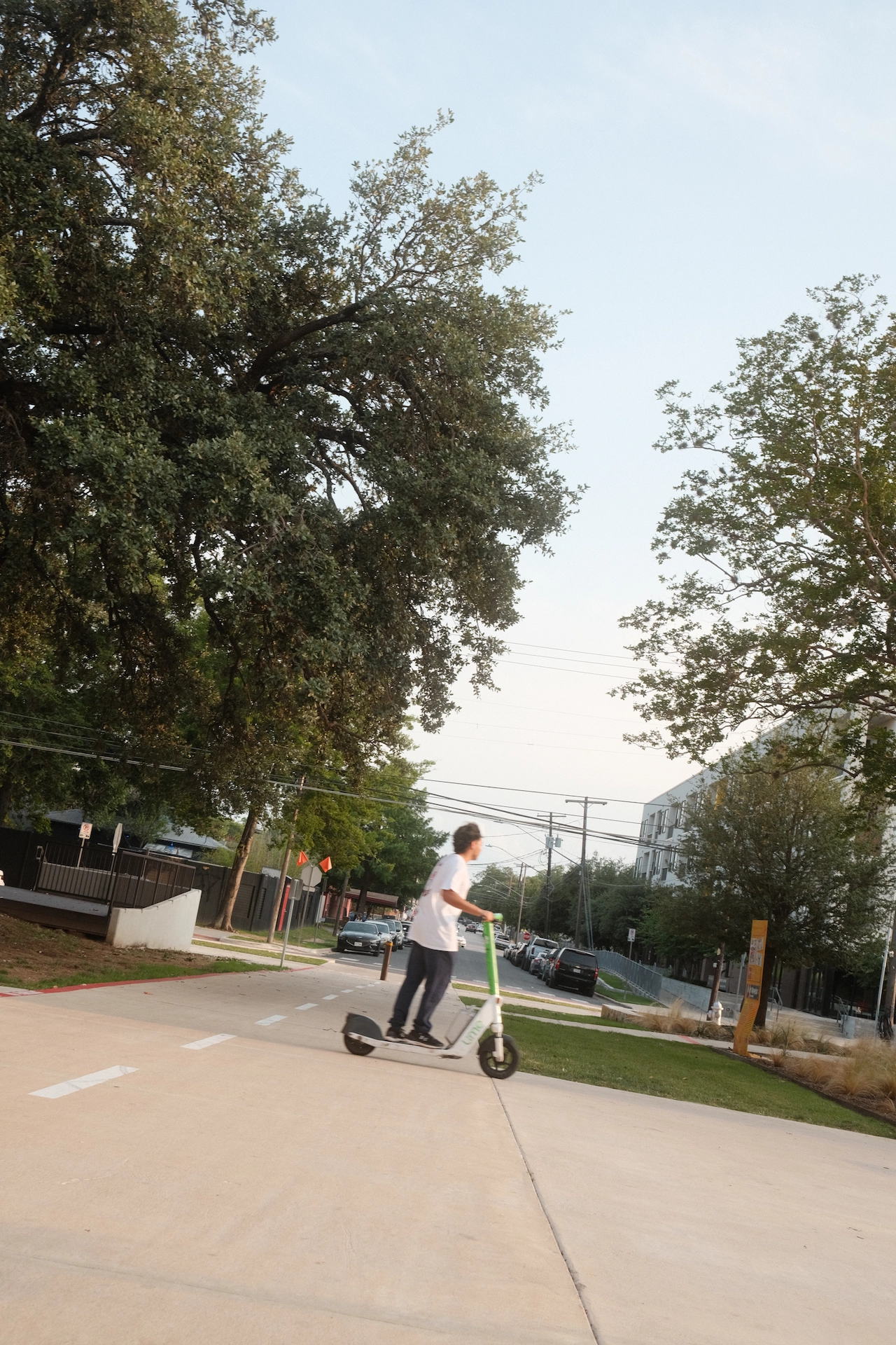 man rides an electric scooter along a city sidewalk bordered by colorful murals and urban greenery, with a relaxed and casual atmosphere