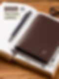 Brown top-grain leather wallet with RFID protection (8 cm x 1 cm x 11.5 cm), displayed on an open notebook with a pen and glasses.