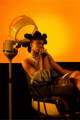 A black model with an exaggerated hairstyle is sitting on a vintage salon chair while holding a NOIRANCA handbag Patti