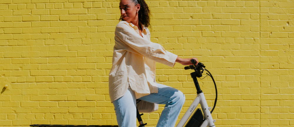 a woman on a Specializd Globe Haul electric cargo bike in front of a yellow brick wall